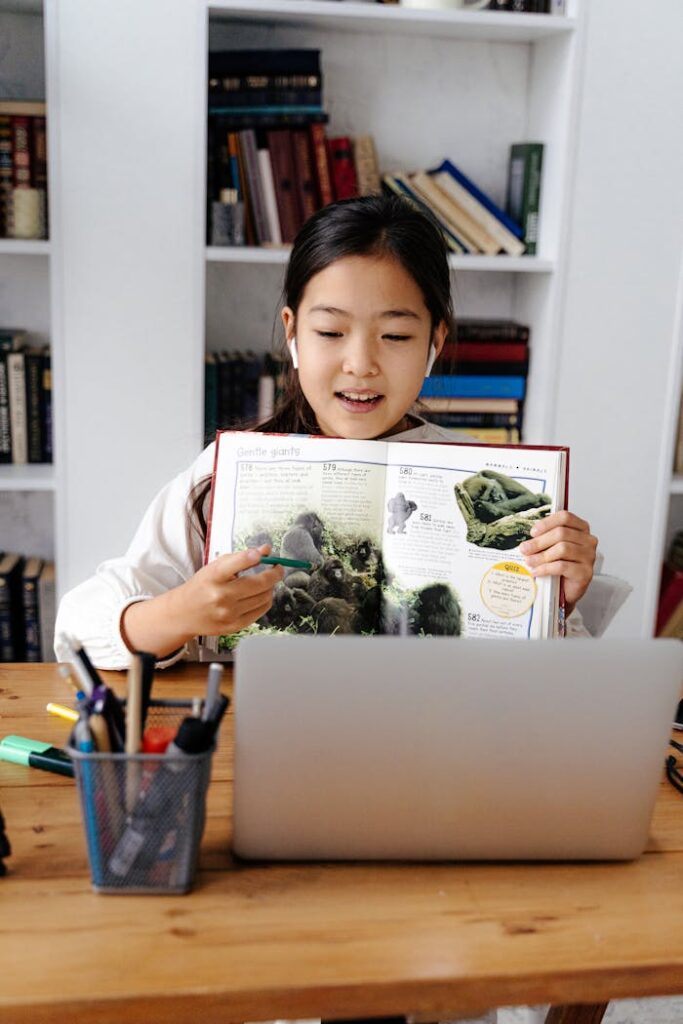 Girl studying online with a laptop and book, illustrating virtual education.